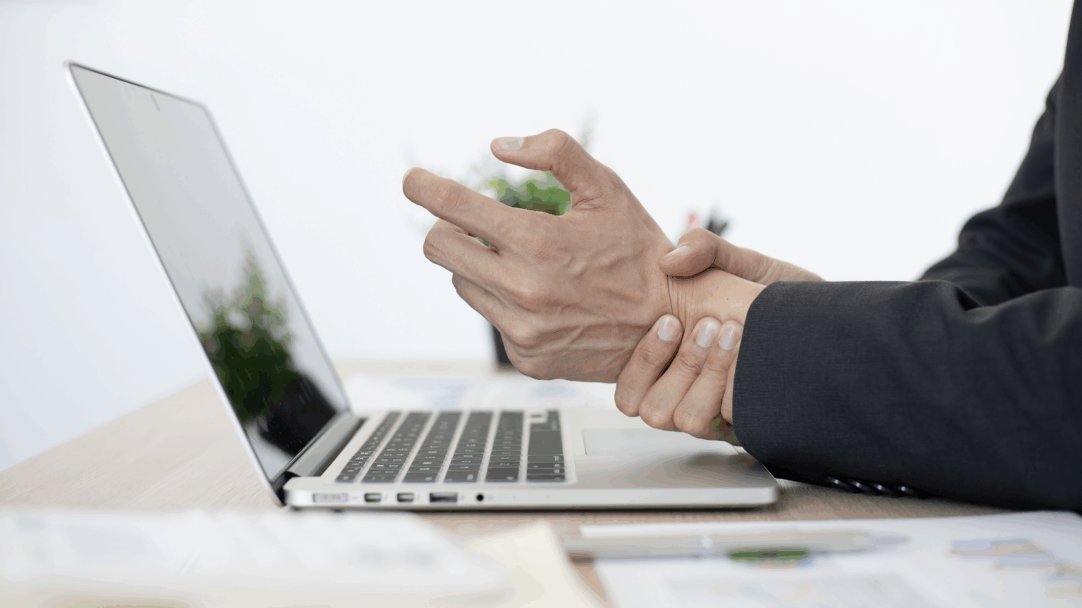 Overworked professional holding wrist pain while sitting in his desk.